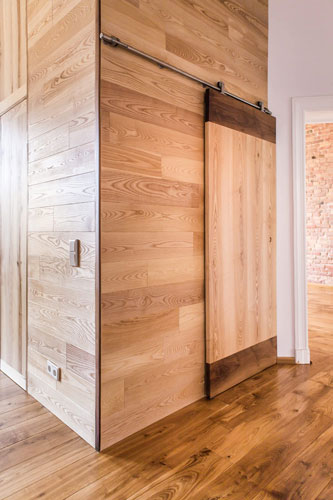 Wooden interior partition wall with large solid wood slide door. Combination of dark and light wood. Solid wooden floor. Design patterns.